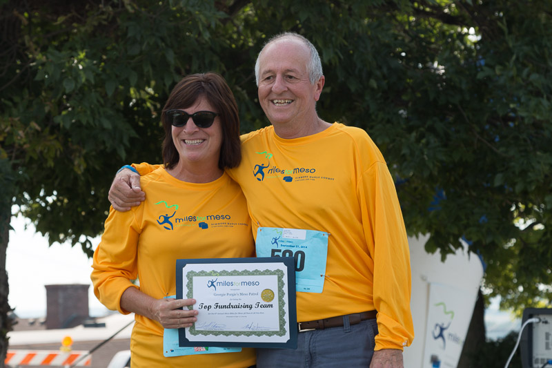 George's family wearing yellow Miles for Meso shirts while holding up a certificate that reads Top Fundraising Team