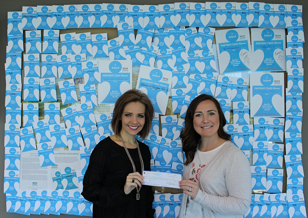 Two employees in the SHC Foundation stand with a check before a wall covered in blue and white hearts