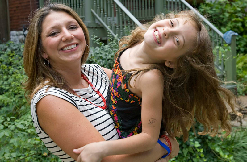 Julie, a mesothelioma survivor, holds her young daughter as they smile together for a photo
