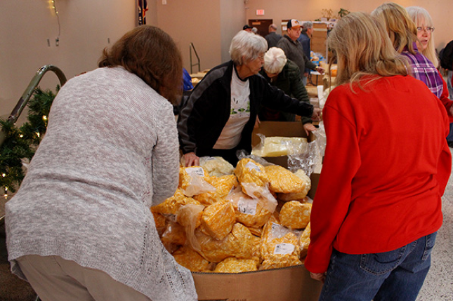 Volunteers set up boxes of cheese for the food basket assembly line.