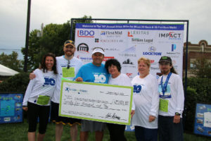 A group holds a large check at the annual Miles Meso 5K