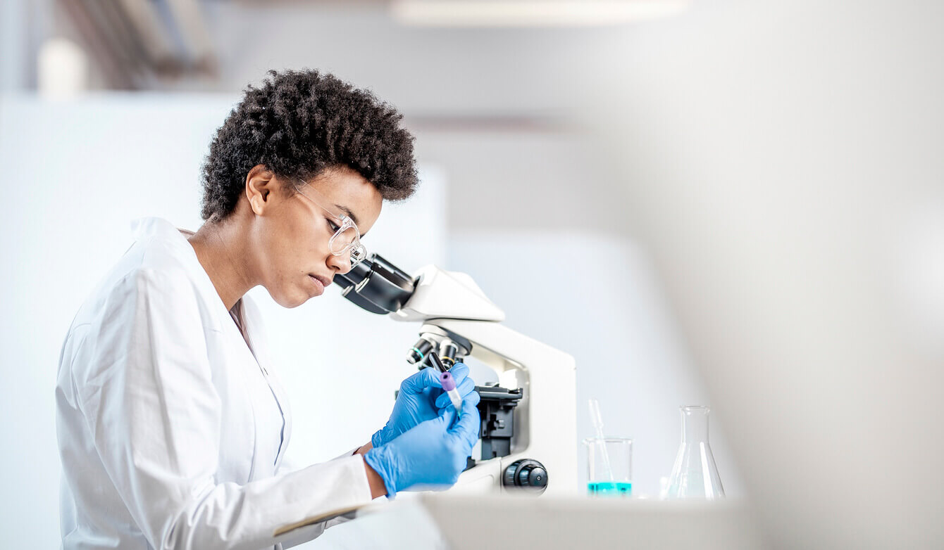 A lab technician looks into a microscope