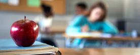 Apple on a teacher's desk with blurred students in background