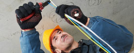 An electrician in a yellow hard hat works on wires